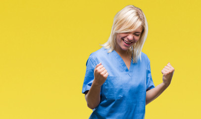 Young beautiful blonde nurse doctor woman over isolated background very happy and excited doing winner gesture with arms raised, smiling and screaming for success. Celebration concept.