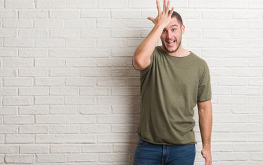 Young caucasian man standing over white brick wall surprised with hand on head for mistake,...