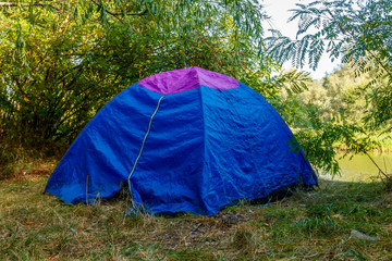 Blue camping tent in forest near a river