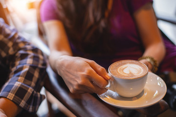 Youngg woman with friend hands holding with latte coffee on a wood table in coffee shop ,relax and vacation concept.