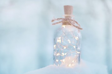 Winter time.Magic Christmas garland.Glass bottle with shining garland in the snow on a blurred...