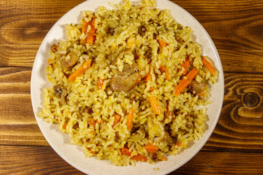 Pilaf with meat, rice, carrot and onion in a plate on wooden table. Top view