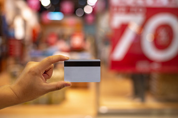Closeup of green credit card holded by hand on blurred shop mall background ,copy space.