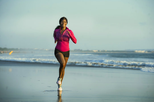 young happy and attractive African American runner woman exercising on running workout at beautiful beach jogging and enjoying sunset in outdoors activity fitness concept