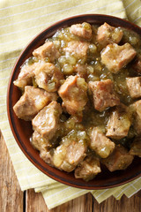 Pork slowly stews with jalapenos, onion, green verde sauce and spices in this flavor-packed Mexican dish closeup on a plate. Vertical top view