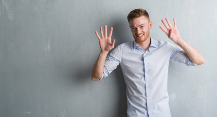 Young redhead business man over grey grunge wall showing and pointing up with fingers number nine while smiling confident and happy.