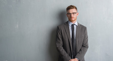 Young redhead elegant business man over grey grunge wall with a confident expression on smart face thinking serious