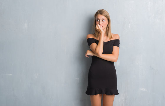 Beautiful young woman standing over grunge grey wall wearing elegant dress looking stressed and nervous with hands on mouth biting nails. Anxiety problem.