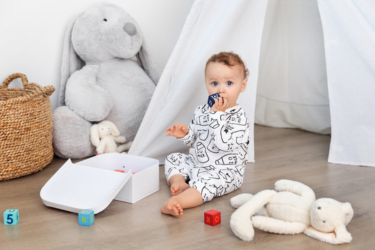 Cute toddler sitting on playroom floor chewing on blocks
