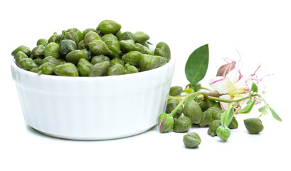 Capers, green leaves and caper flower in white bowl on white background