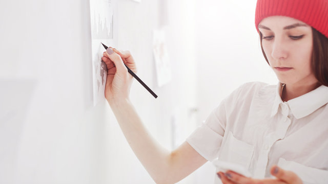 Young hipster lady working on analitical reports, making notes on graphics