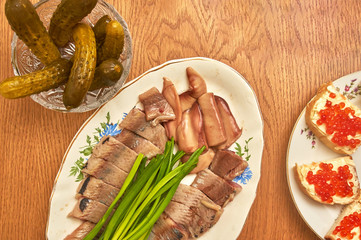 Herring with green onions in a salad bowl on a wooden table, top view