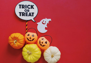 Flat lay of halloween props with pumpkins and trick or treat word on red background, holiday concept