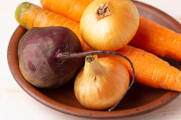 Onions, carrots and beets in a clay plate close-up. Preparing fresh vegetables for cooking