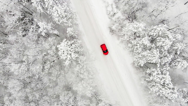 rotes Auto auf einer schneebedeckten eisigen Stra&szlig;e im Winter von oben, Luftbildaufnahme