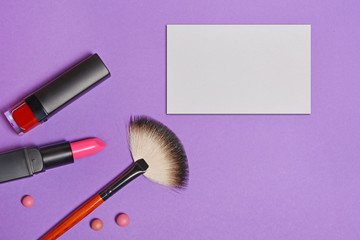 Top view on set of beauty products for makeup and mock-up business card on purple background
