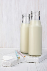 Classic glass bottles of milk and cocktail straws on white wooden board