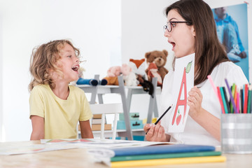 A happy child pronouncing a letter during speech therapy with a specialist.