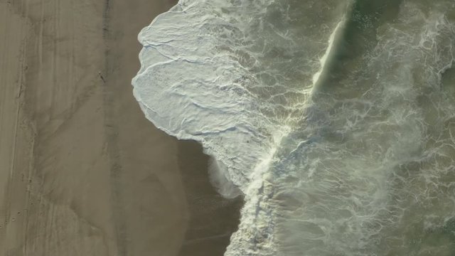 Birdseye view of waves crashing against rocks on the beach.