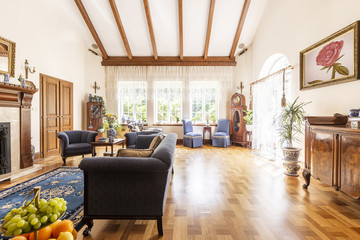A view of a luxurious high ceiling living room interior with wooden floor, sunny windows and...