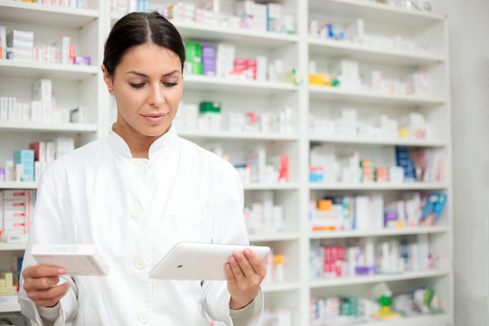 Medicine, pharmaceutics, health care and people concept - Young pharmacist holding a tablet and box of medications.