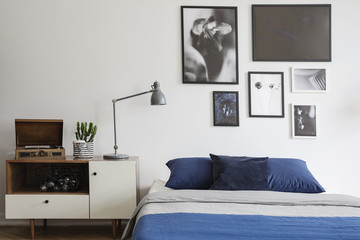 Scandinavian style, wooden dresser by a navy blue bed and framed art gallery on a white wall of a...
