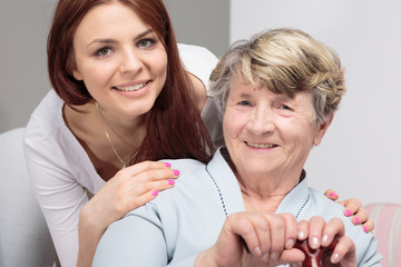 Smiling daughter hugging happy senior mother with walking stick during meeting