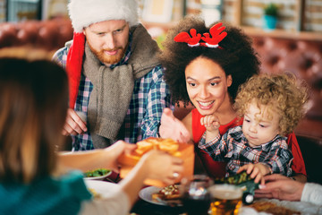 Man and mixed race woman giving toddler Christmas gift while sitting at table. Christmas holidays concept.