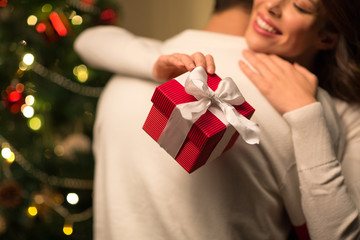winter holidays and people concept - close up of happy couple with christmas gift hugging at home