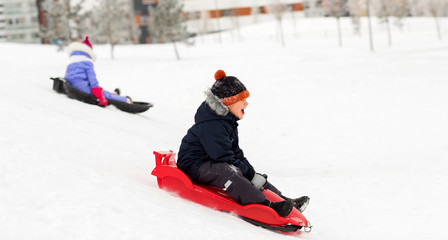 Fototapeta na wymiar childhood, sledging and season concept - happy little kids sliding on sleds down snow hill in winter