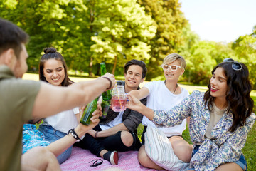 leisure, people and celebration concept - happy friends clinking non alcoholic drinks at picnic in summer park