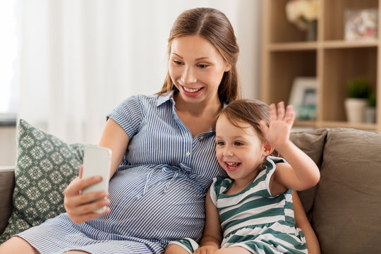 pregnancy, technology and family concept - happy pregnant mother and little daughter having video chat on smartphone at home