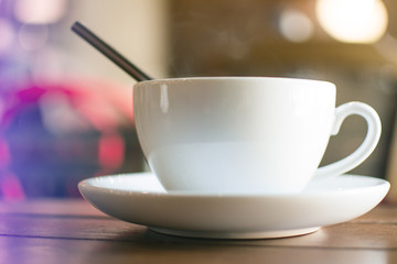 A white cup of hot coffee with steaming on the wooden table