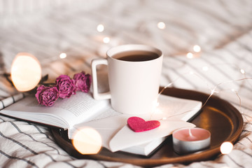 Cup of tea staying on open book with flowers and lights at background. Valentines day. Good morning.