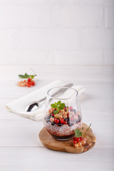 Chia pudding with fresh currant berries in glass on white table.