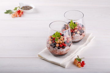 Chia pudding with fresh currant berries in glass on white table.