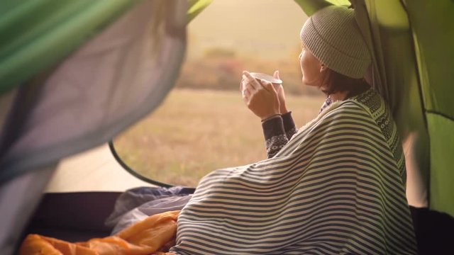 Woman drinks hot tea in camping tent and enjoy with autumn evening in mountain valley