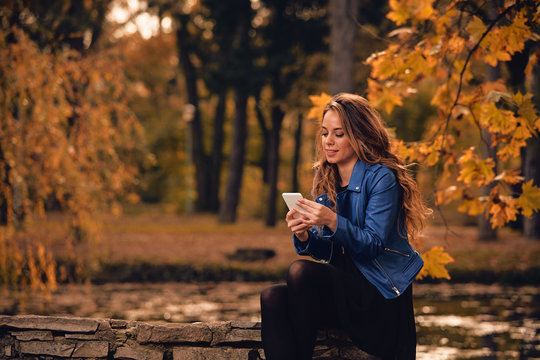 Cute girl using cellphone in park with autumn colors.