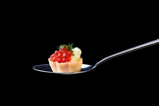 Tartlet with red caviar and butter and dill on a tablespoon on a black background
