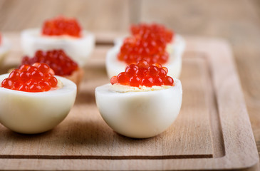 Selective focus. Red caviar on halves of hard-boiled chicken eggs on a cutting board © svdolgov