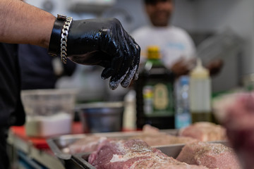 Protein and iron based diet. Gourmet chef, salting and spicing steaks, chops, burgers and fillets for the homeless and poor on Christmas Eve. Black rubber gloves, sharp knife.