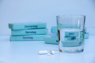 Medikamente, Kapseln, Tabletten und Wasserglas auf einem weißen Tisch