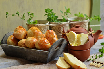 Fluffy buns in a wooden basket. Butter in a clay bowl on a wooden background