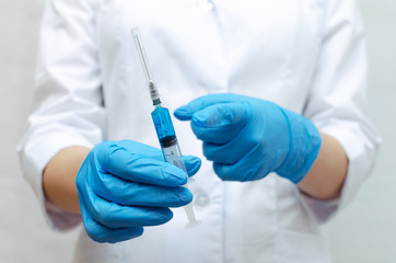 Syringe with a blue medical drug in the doctor hands dressed in the medical gown. Medical drug presentation concept.