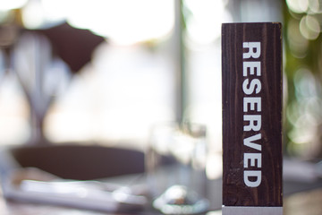 Reserved wooden Card Plate on the Table with Blurry background. Reservation Seat at restaurant. - leisure, people and service concept