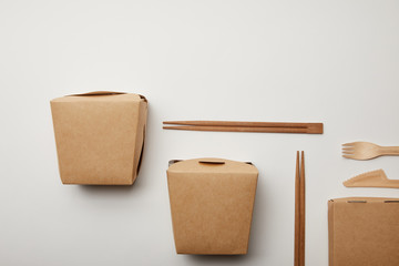 elevated view of arranged wok boxes, chopsticks and disposable knife with fork on white surface