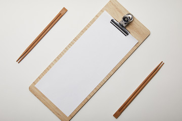 elevated view of arranged blank menu and chopsticks on white surface, minimalistic concept
