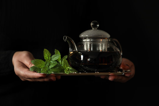 Teapot of spearmint tea on a tray in the hands of a woman.