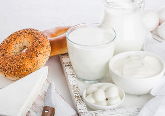 Fresh dairy products in vintage wooden box on white table background. Jar and glass of milk, bowl of sour cream and cheese. Fresh baked bagels. Space for text