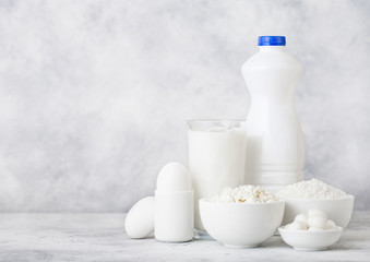 Fototapeta na wymiar Fresh dairy products on white table background. Plastic bottle and glass of milk, bowl of cottage cheese and baking flour and mozzarella. Eggs and cheese.